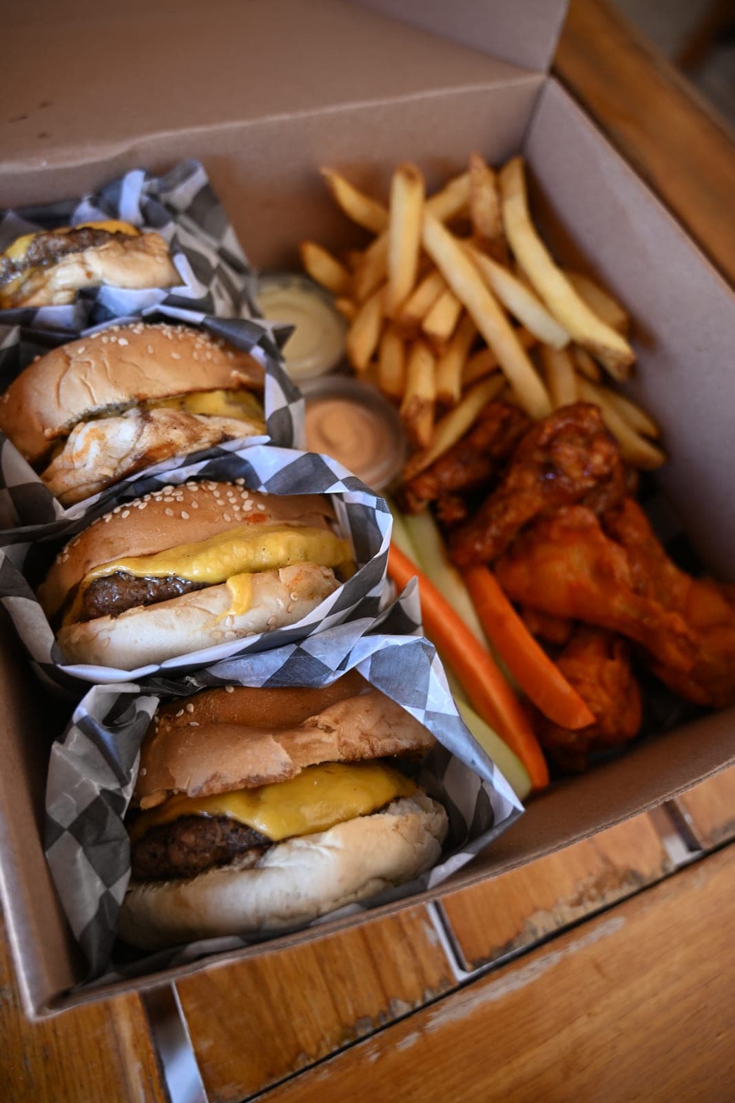 Una caja para llevar con cuatro hamburguesas, papas y alitas
